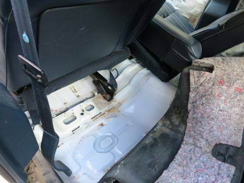 1991 Ford LTD Crown Victoria - The interior rear floor of a vehicle shows exposed white metal and a black seatbelt, with some signs of wear and tear.