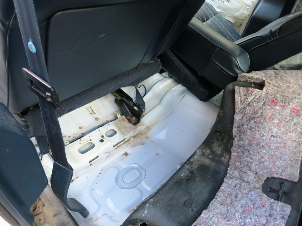 Interior rear floor with exposed white metal and black seatbelt