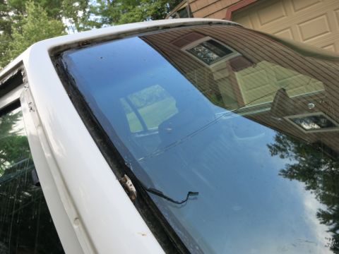 1991 Ford LTD Crown Victoria - The weathered windshield frame and glass of a white vehicle are visible, with reflections of a house in the background.