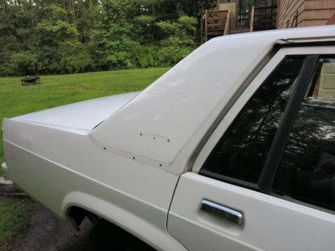 1991 Ford LTD Crown Victoria - Close-up of the rear quarter panel and roofline of a white sedan, showing screw holes where trim may have been removed.