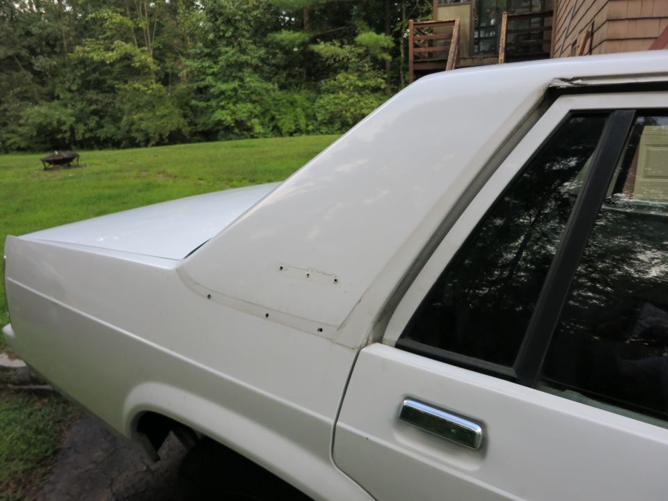 White sedan rear quarter panel and roofline with visible screw holes