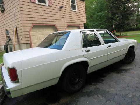 1991 Ford LTD Crown Victoria - A white sedan is parked on a driveway in front of a house with a garage.