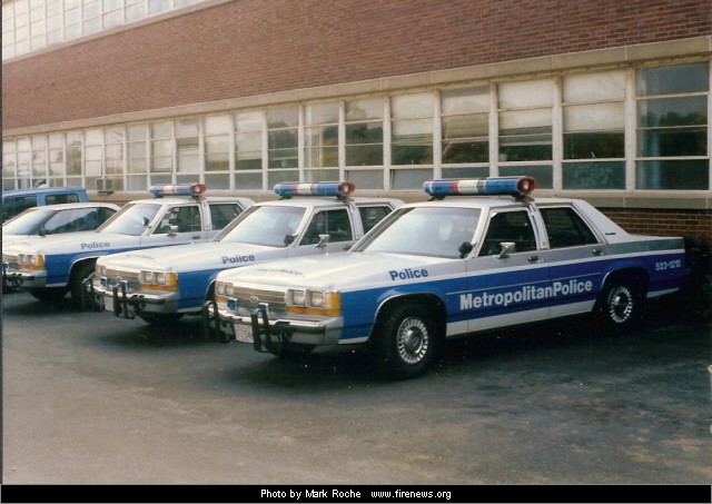 Several police cars parked in a row in front of a brick building. They have 'Metropolitan Police' written on the side