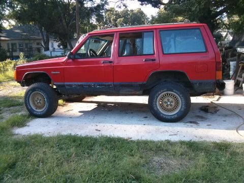 1986 Ford Bronco - Side view of a red Jeep Cherokee SUV, likely from the 1980s, with custom wheels.