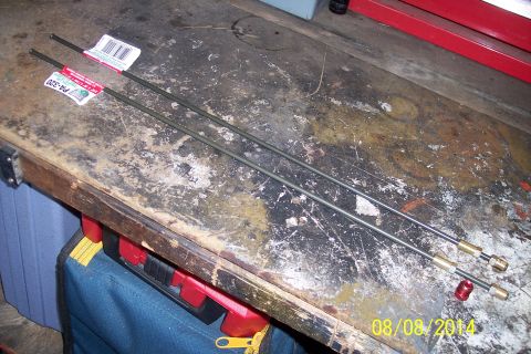 1978 Ford Bronco - Two metal brake lines with brass fittings and red caps are laid out on a cluttered workbench.