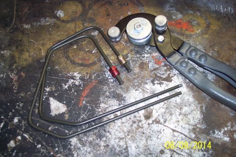 1978 Ford Bronco - A tubing bender and pre-bent metal tubes are laid out on a workbench surface.