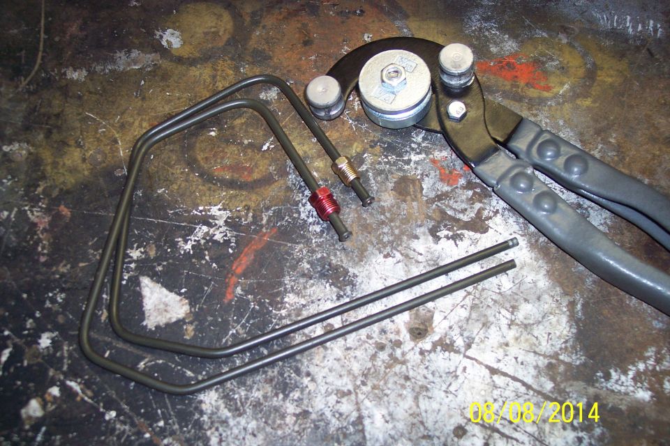 Tubing bender tool with two bent metal tubes and fittings on a workbench