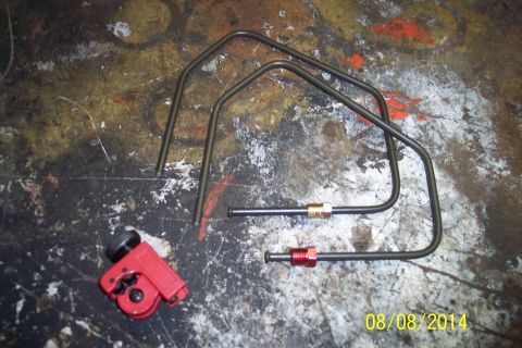 1978 Ford Bronco - A red tubing cutter and two pre-bent brake lines are laid out on a stained workbench surface.