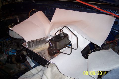 1978 Ford Bronco - A brake master cylinder is placed in a foil pan, surrounded by paper towels, within a vehicle's engine compartment.