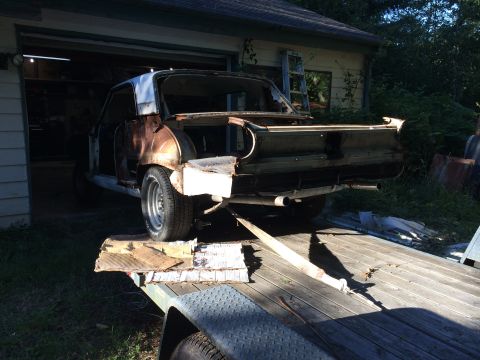 1964 Ford Fairlane - The rear of a heavily rusted car, stripped down and being loaded onto a trailer for transport.