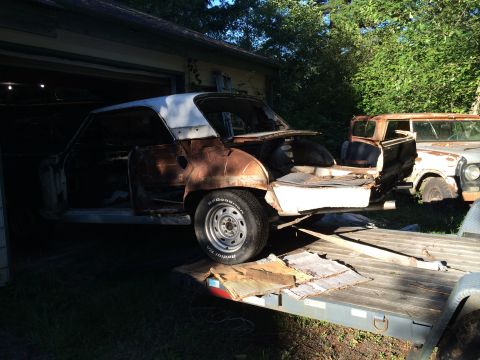 1964 Ford Fairlane - A heavily rusted car, stripped down and on a trailer, with another vehicle in the background.