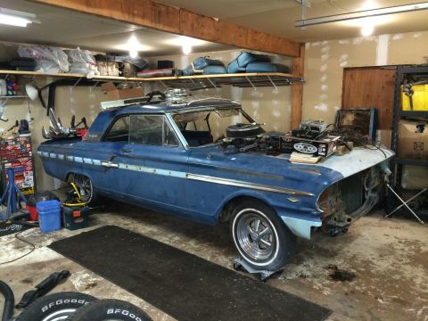 1964 Ford Fairlane - A blue 1964 Ford Fairlane sits in a garage, appearing to be in the process of restoration with various parts and equipment around it.