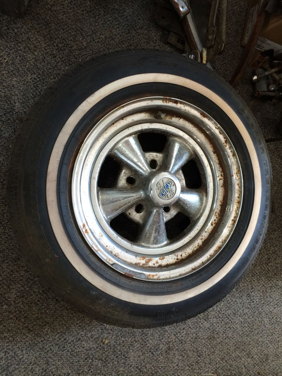 Chrome five-spoke wheel with a whitewall tire. Center cap has text and a logo