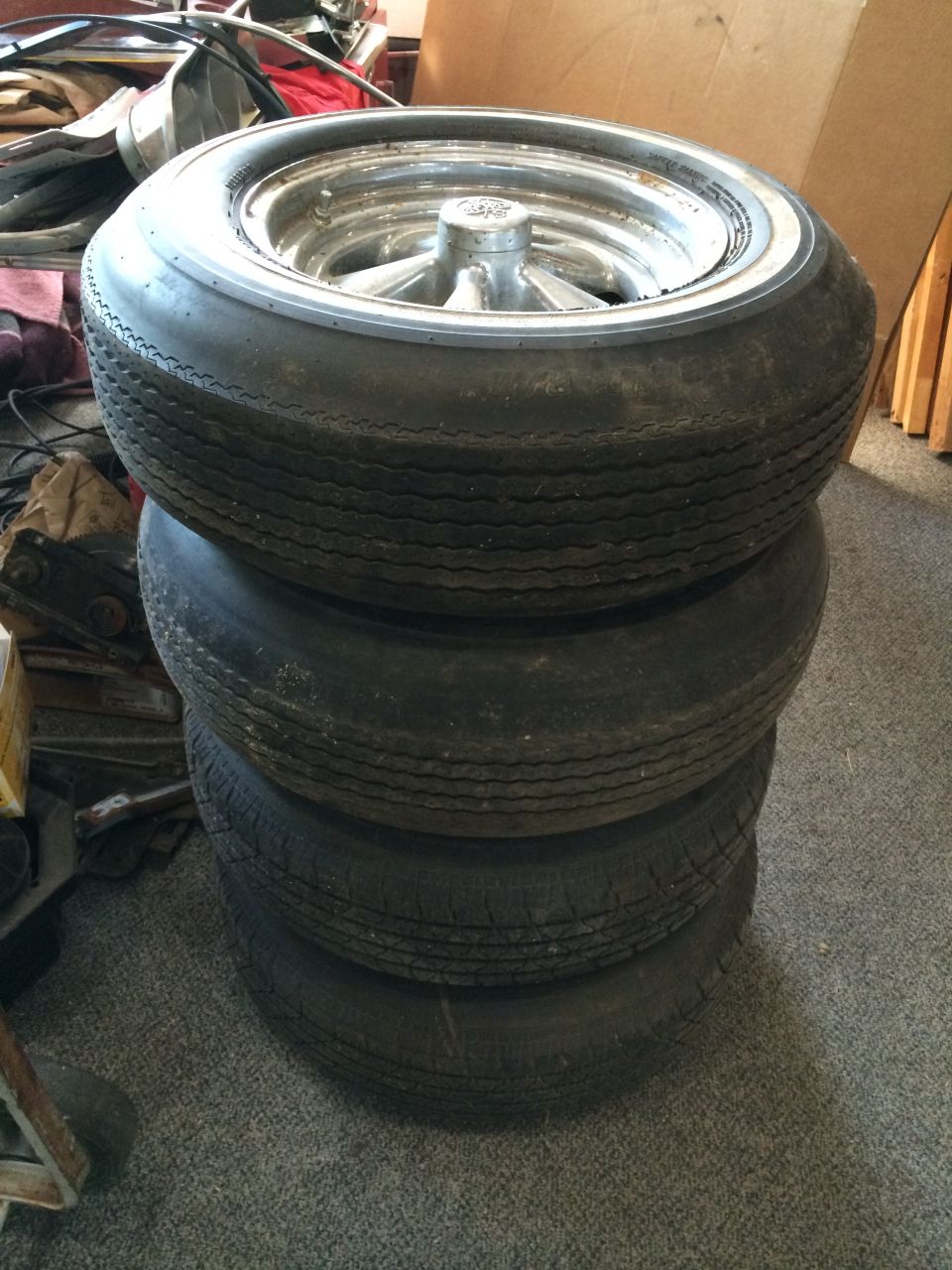 stack of four tires with chrome rims, one tire on top has a white wall