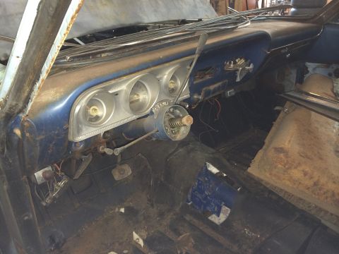 1964 Ford Fairlane - The interior of a vintage car shows a dusty dashboard with gauges and a steering column, indicating a need for restoration.