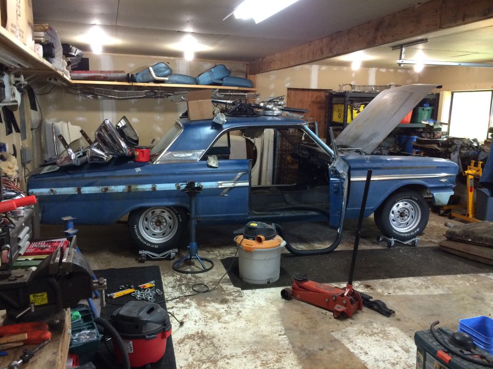 Blue 1964 Ford Fairlane coupe in garage with hood and doors open, parts on roof