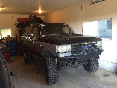 1989 Ford Bronco - This lifted Ford Bronco is parked inside a garage with storage shelves in the background.