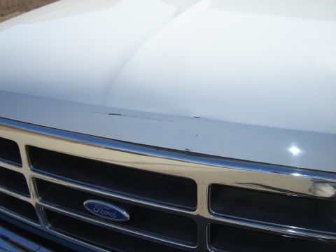 1996 Ford Bronco - Close-up of a white 1996 Ford Bronco's front grille and hood, revealing the Ford emblem and some surface imperfections.