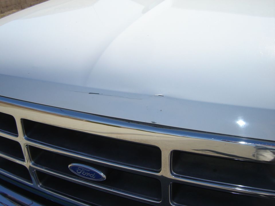 White 1996 Ford Bronco grille with chrome trim and Ford logo; hood shows minor scratches