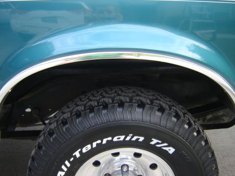 1996 Ford Bronco - Close-up of the rear wheel well on a teal 1996 Ford Bronco, showing the tire and chrome trim.