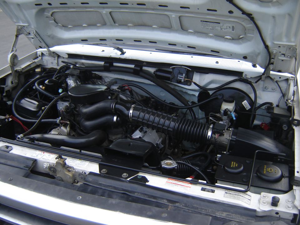 engine bay with hoses, air intake, and various engine components visible