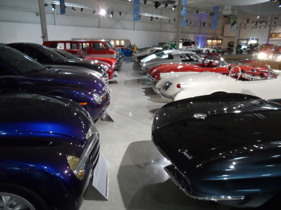 Several classic cars parked in a museum hall, including a red van and a white sports car