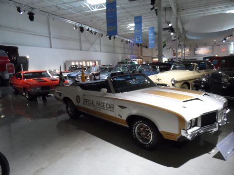 1971 Ford Ranchero - A 1971 Oldsmobile Cutlass Supreme convertible, marked as an official pace car, is displayed indoors among other vehicles.