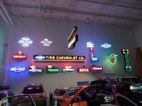 1971 Ford Ranchero - A variety of vintage automotive neon signs are displayed in a showroom above several cars.