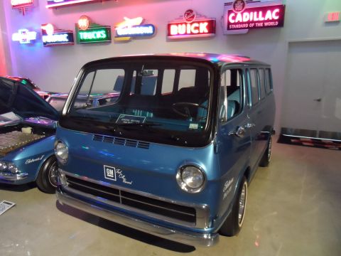 1971 Ford Ranchero - A blue van is displayed indoors, with neon signs for various car brands on the wall behind it.