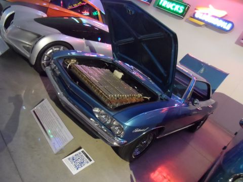 1971 Ford Ranchero - A blue 1967 Chevrolet El Camino is displayed with its hood open, revealing a large battery pack, next to a modern silver car.