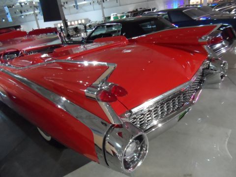 1971 Ford Ranchero - A classic red convertible with distinctive tail fins is displayed indoors, with other vehicles visible in the background.