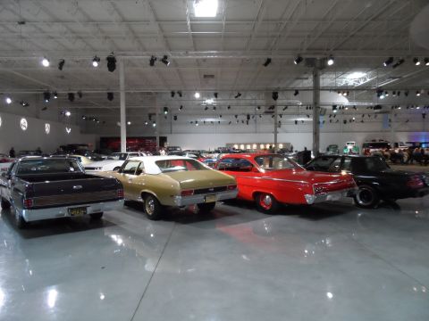 1971 Ford Ranchero - A collection of vintage automobiles are displayed indoors under bright lighting.
