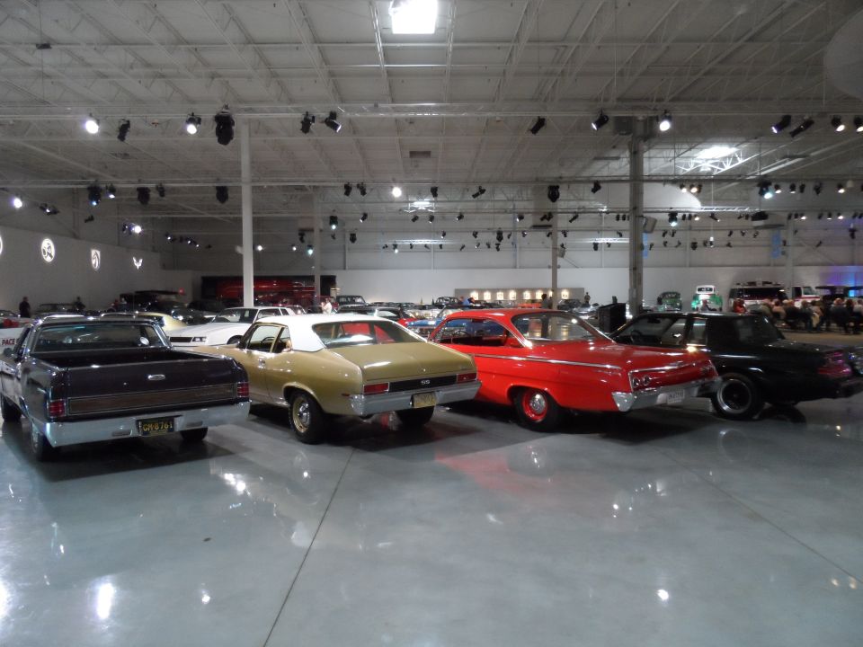 Several classic cars parked in a large indoor space, including a black pickup truck, a gold coupe, and a red sedan