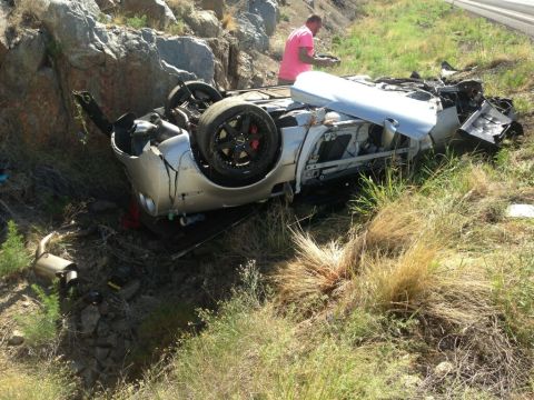 2010 Dodge Challenger - Silver car overturned on its side, damaged, with a person in a pink shirt standing nearby.
