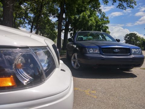 2000 Mercury Grand Marquis - Two vehicles are parked outdoors on a sunny day with trees in the background. The blue car is a Ford Crown Victoria.