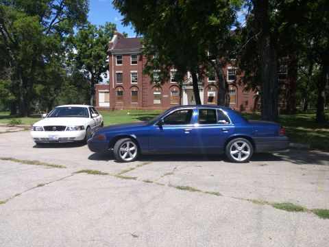 2000 Mercury Grand Marquis - A blue 2000 Mercury Grand Marquis is parked next to a white sedan in front of a brick building.
