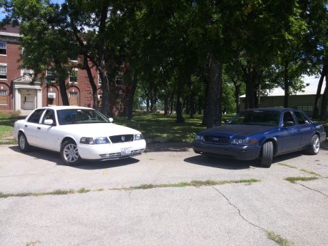 2000 Mercury Grand Marquis - Two sedans, a white 2000 Mercury Grand Marquis and a blue sedan, are parked side-by-side outdoors.