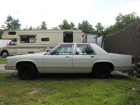 1991 Ford LTD Crown Victoria - A white sedan is parked on grass next to an RV and a trailer.