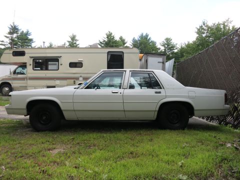 1991 Ford LTD Crown Victoria - A white 1991 Ford Crown Victoria LTD sedan is parked on grass next to an RV and a fence.