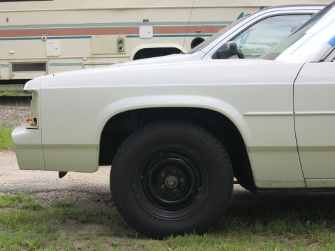 1991 Ford LTD Crown Victoria - The front fender and wheel well of a white sedan are visible, with an RV in the background.