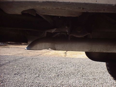 1988 Ford Bronco - The underside of a vehicle's exhaust system is visible, with a wire hanging from the pipe.