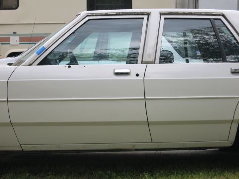 1991 Ford LTD Crown Victoria - Side view of a white sedan with chrome door handles and trim. Blue tape is visible on the driver's side window frame.