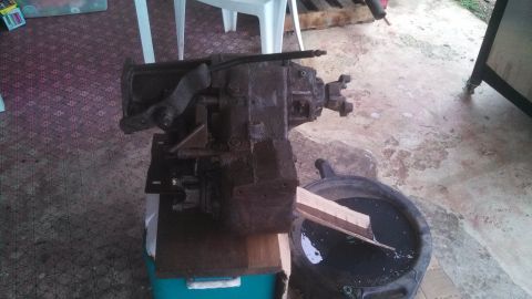 1979 Ford Bronco - A transmission assembly is shown, resting on wooden blocks beside a pan filled with dark fluid.
