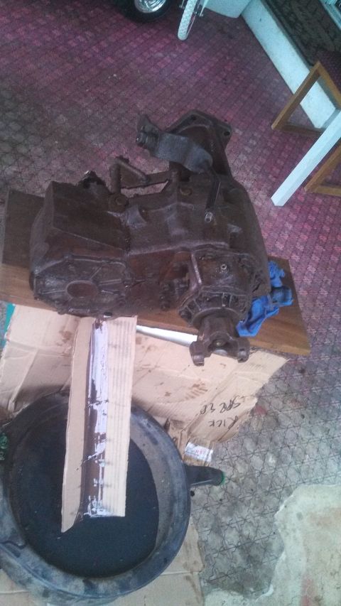 1979 Ford Bronco - A rusty transfer case sits on a wooden plank over cardboard, with a blue cloth nearby.