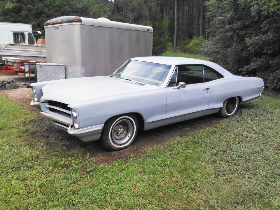 1967 Pontiac Catalina, primer gray, parked outside next to a trailer