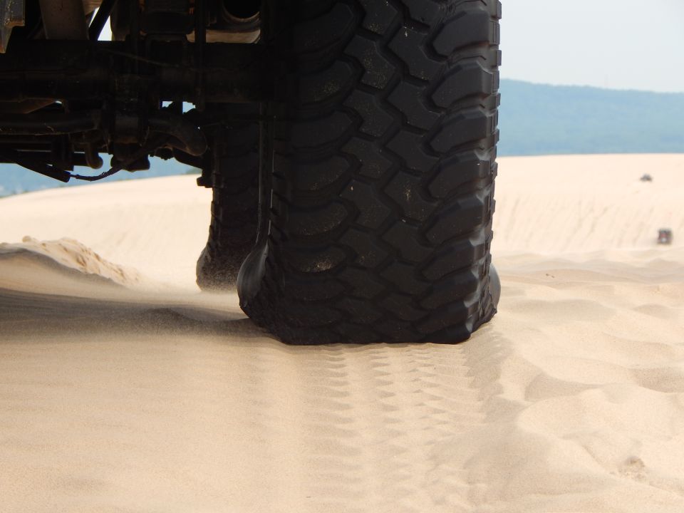 Close-up of a large off-road tire with sand blowing around it