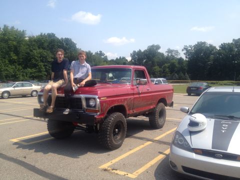 1978 Ford Bronco - This red 1978 Ford Bronco features a lifted suspension and off-road tires, with two individuals casually perched on its hood.