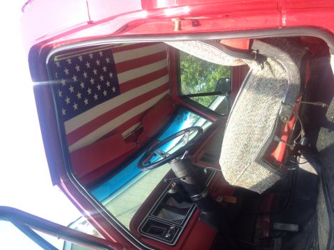 1978 Ford Bronco - Interior of a red truck cab an American flag sunshade and a patterned seat.
