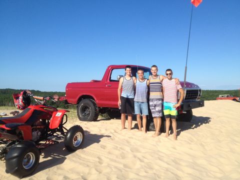 1978 Ford Bronco - A group of friends pose with a red Ford Bronco and an ATV in a sandy, outdoor setting under a clear blue sky.