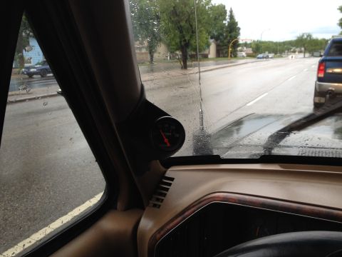 1989 Ford Bronco - A gauge is mounted on the A-pillar inside a vehicle, with a wet road and other vehicles visible through the window.
